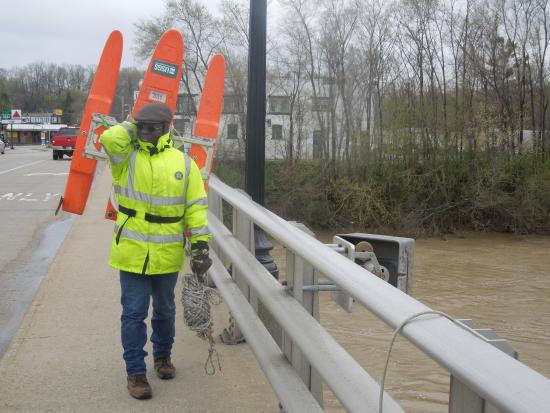 USGS employee using water monitoring equipment over a bridge in an urban area