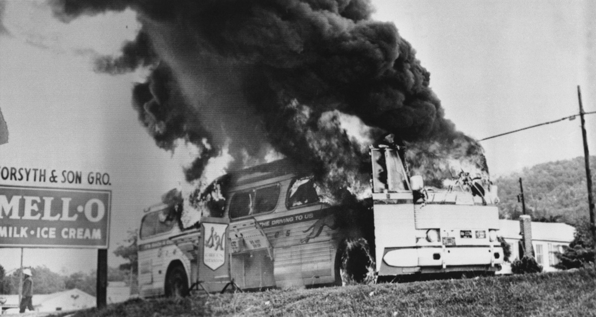An old photo of a greyhound bus burning by the side of a highway.
