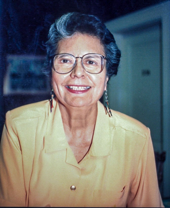 Ada Deer wearing yellow shirt and glasses smiles into the camera.
