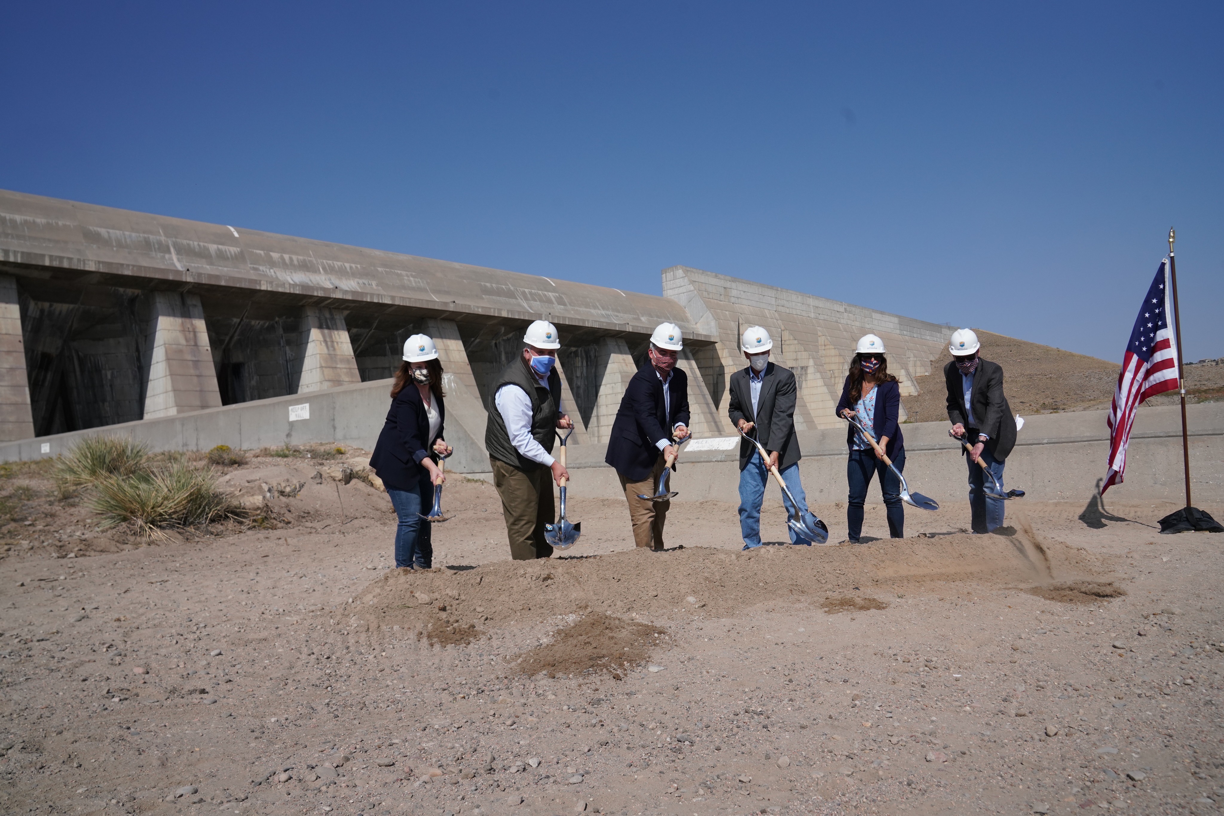 A small group of people use ceremonial shovels for a groundbreaking ceremony outside.