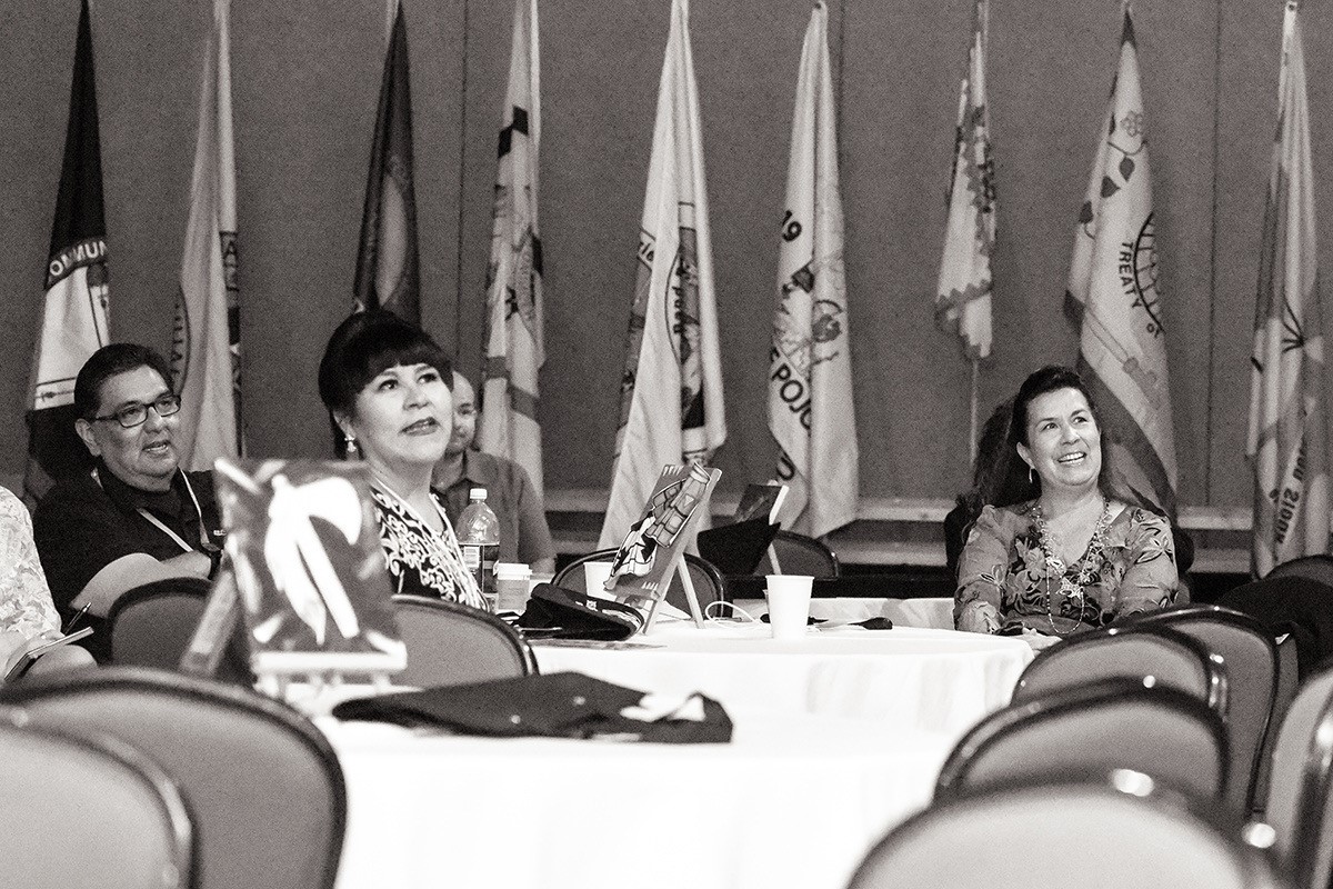 Group of people sit at a table with flags in the background.