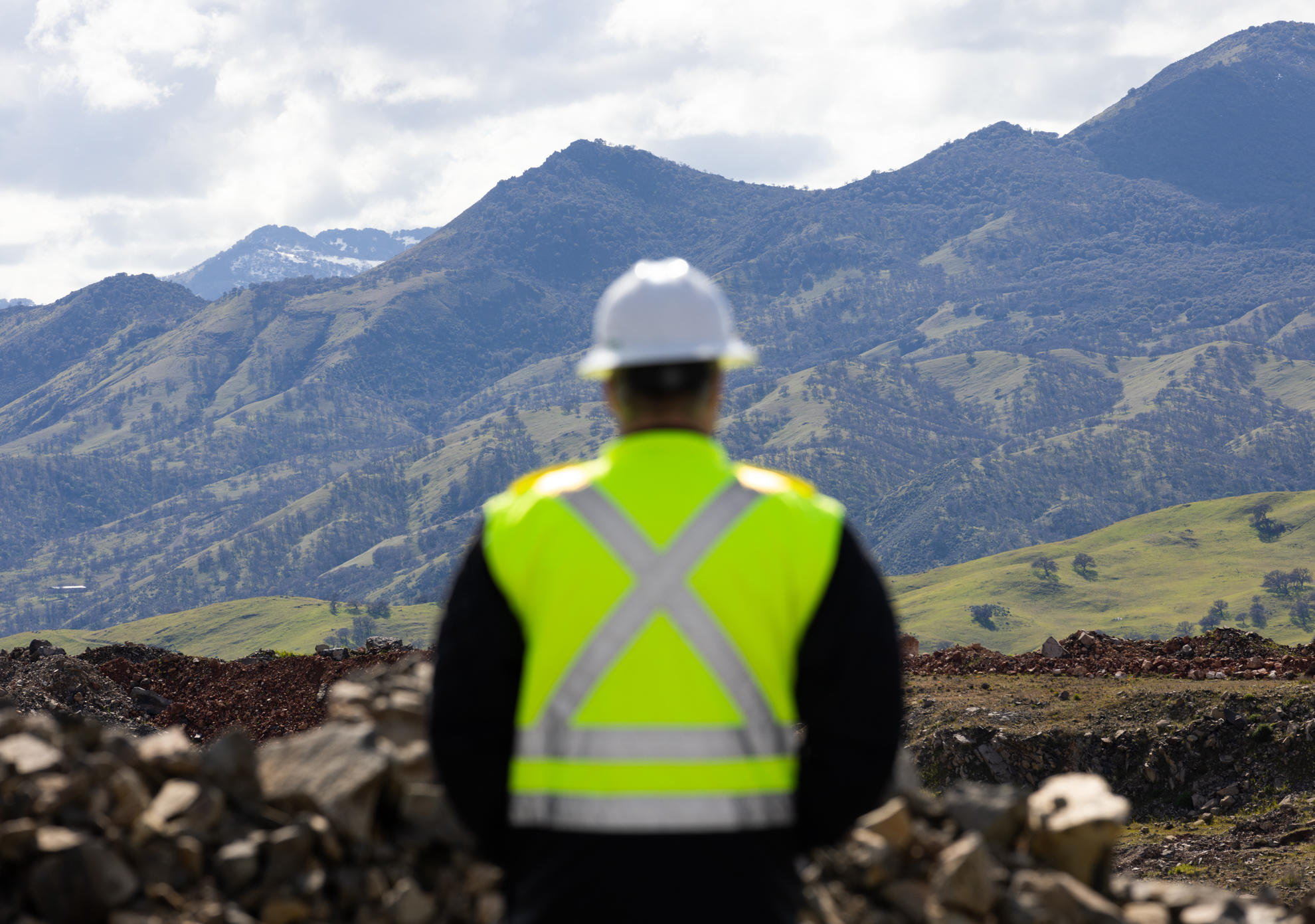 Person in construction vest and hard hat looking out towards landscape. 