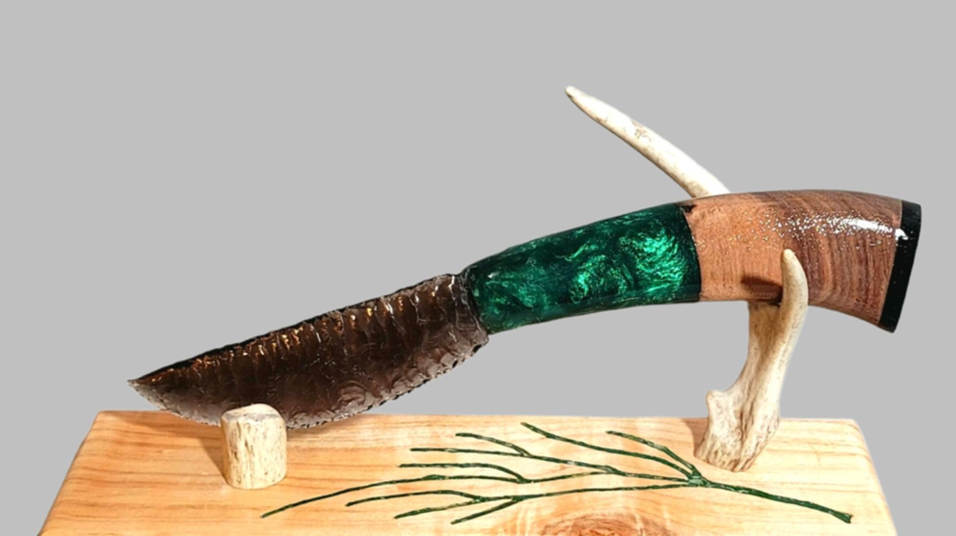 Photograph of an obsidian blade knife with a green handle on a stand made of wood and antlers.
