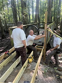 Three MAT members building out an elevated boardwalk surrounded by trees