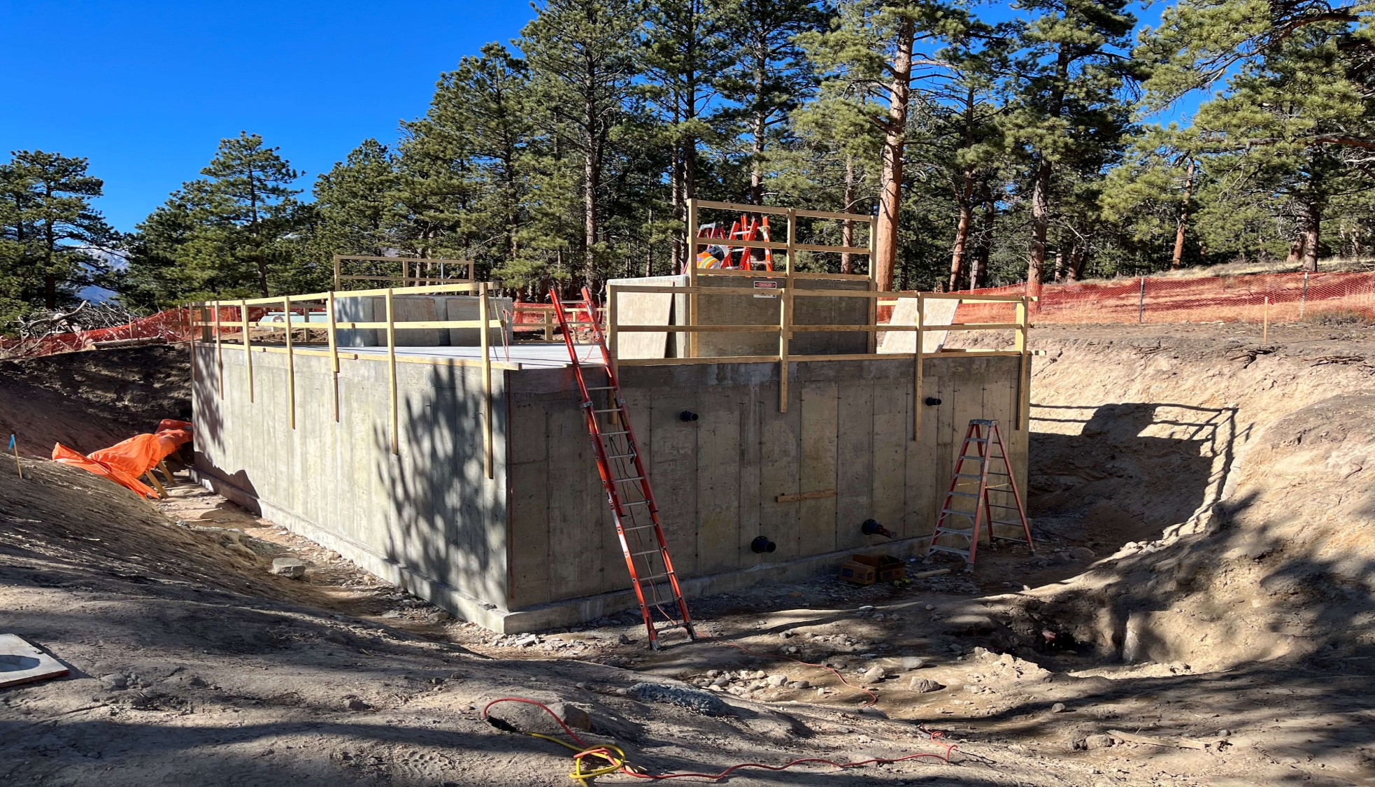 Concrete water tank sits in a dirt hole surrounded by temporary orange fencing.