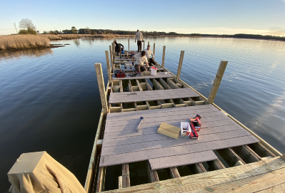 Wooden dock under construction with four workers laying horizontal planks