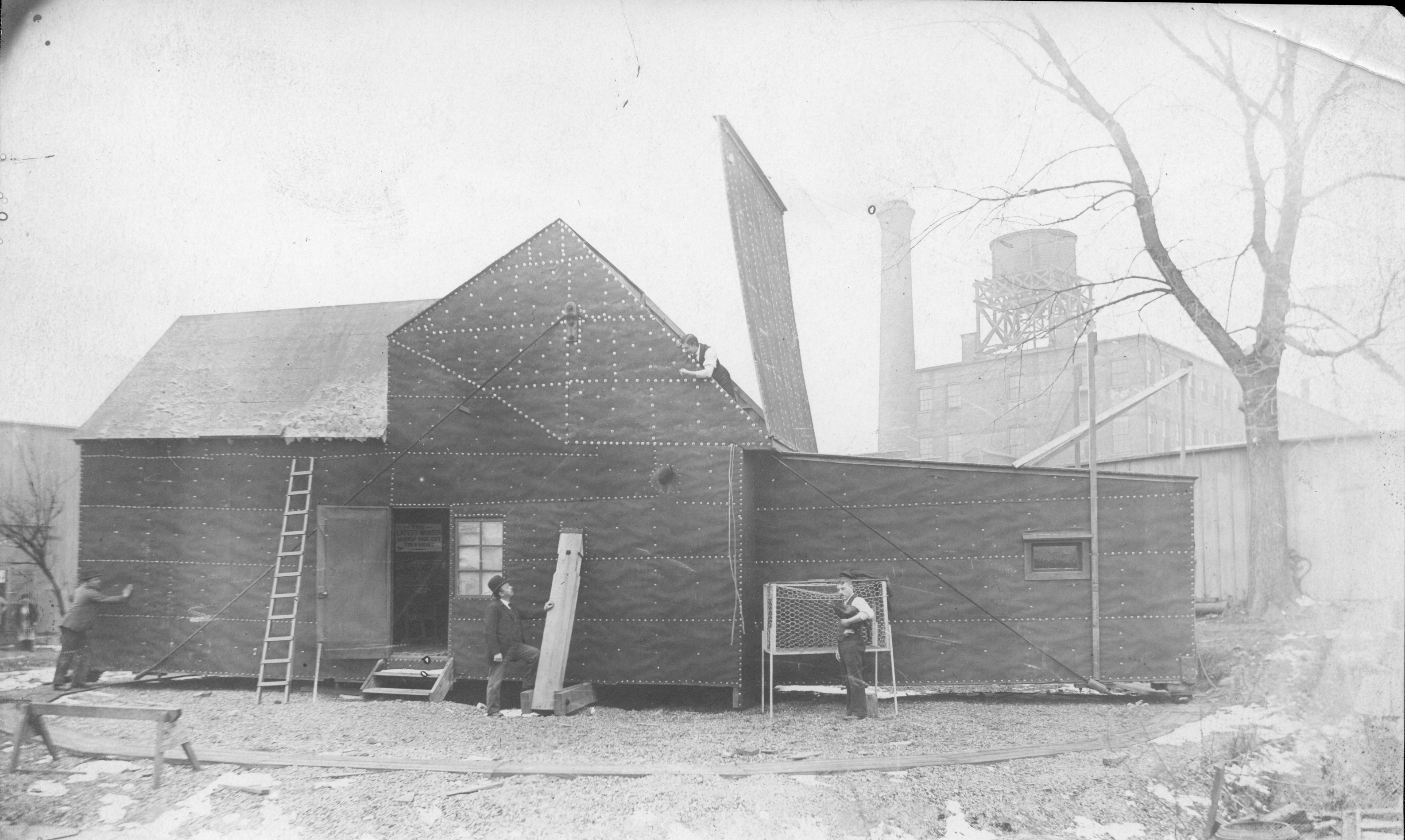 A historic photo of black papered building used as a film studio with workers nearby. The original "Black Maria" with several Edison employees.