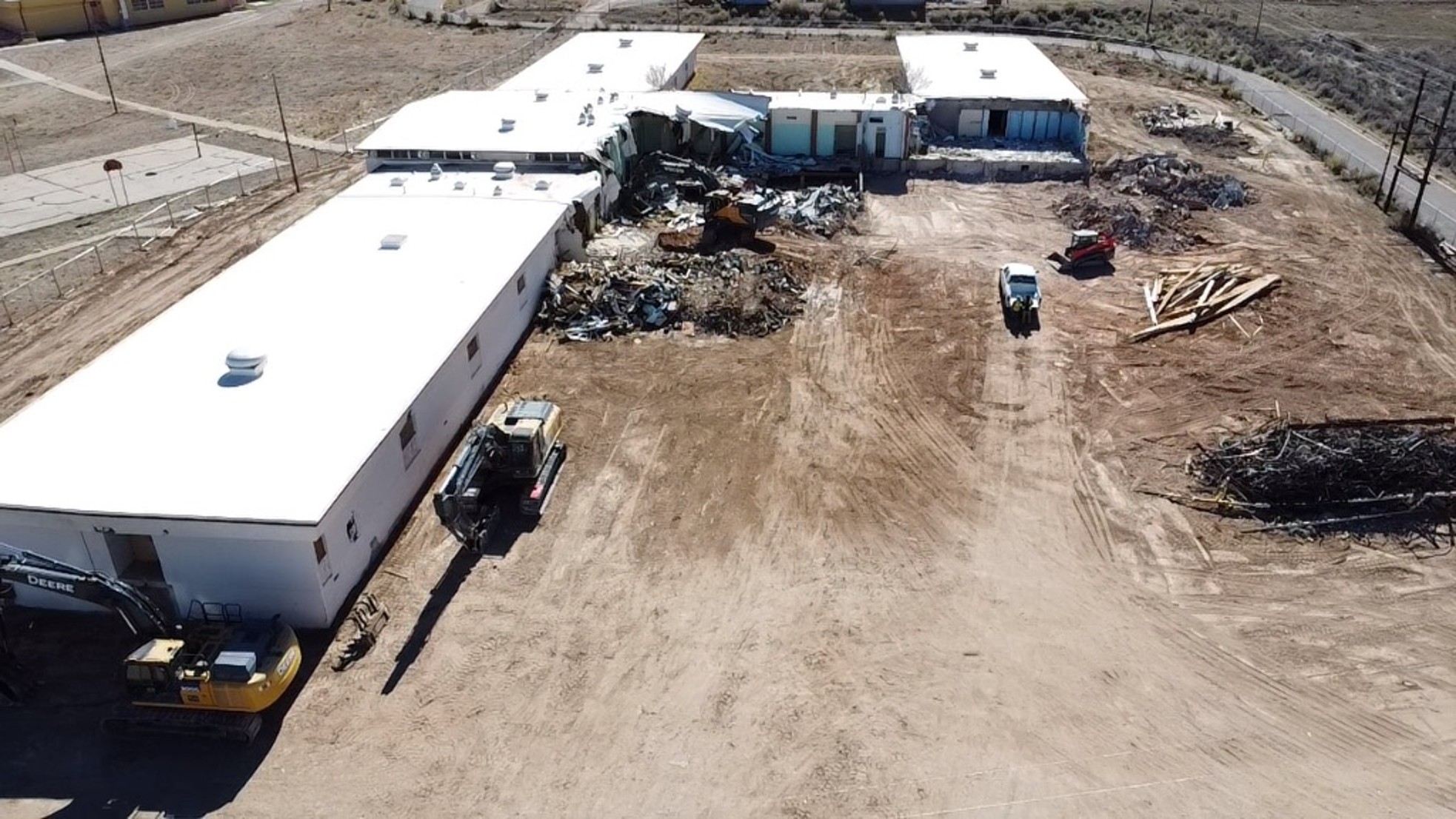 Three excavators demolish building on dirt plot at T’iis Nazbas Community School.