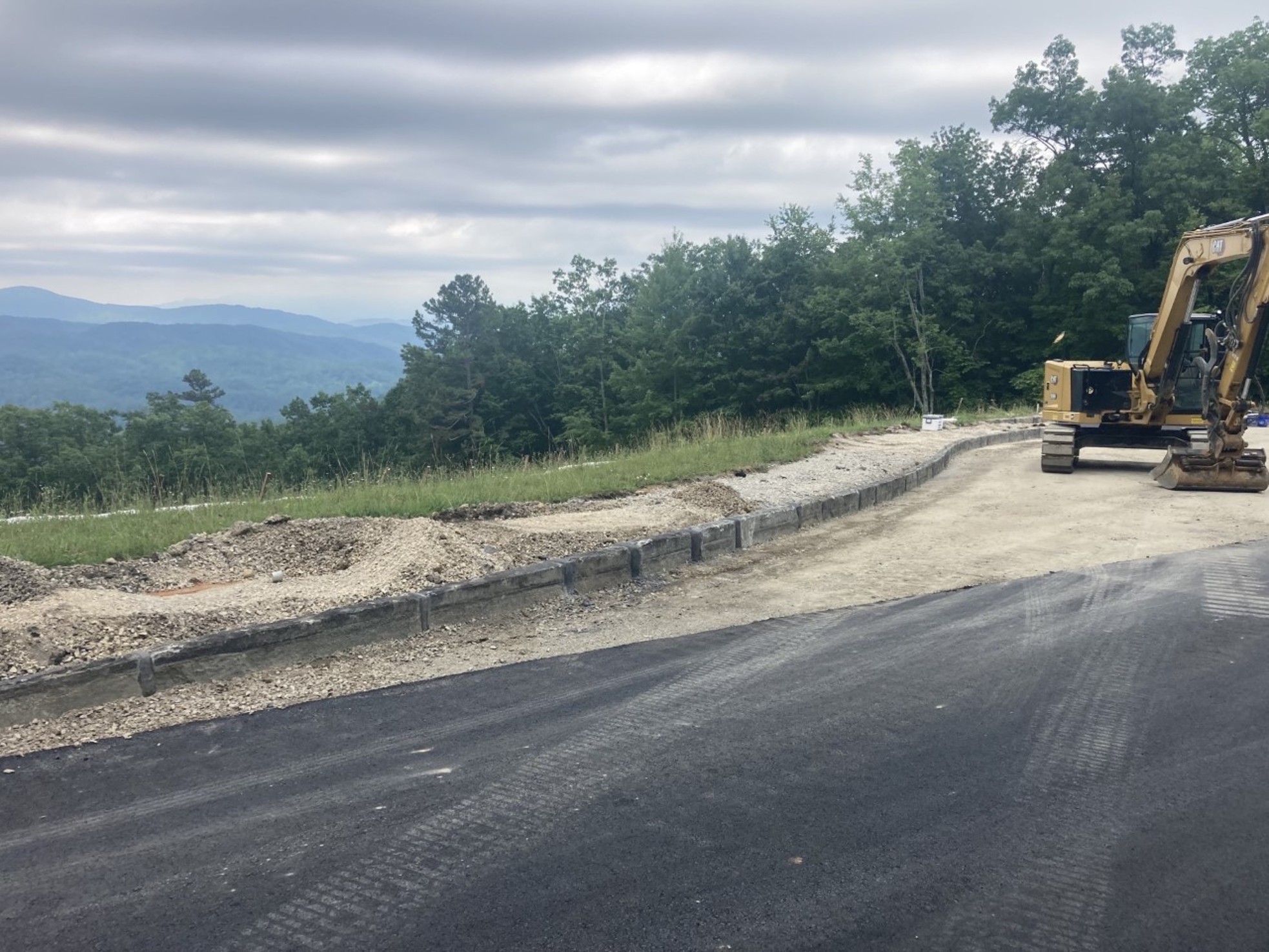  Excavator sits on dirt pullout along paved road, trees line the backgrouns