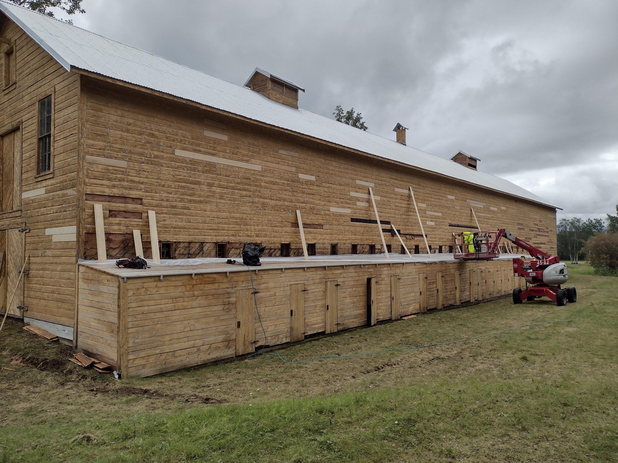 Man in yellow construction suit replaces wooden boards on the side of a barn.