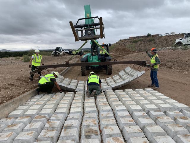 Men in yellow construction vests use a fork lift to install mats on dirt road.