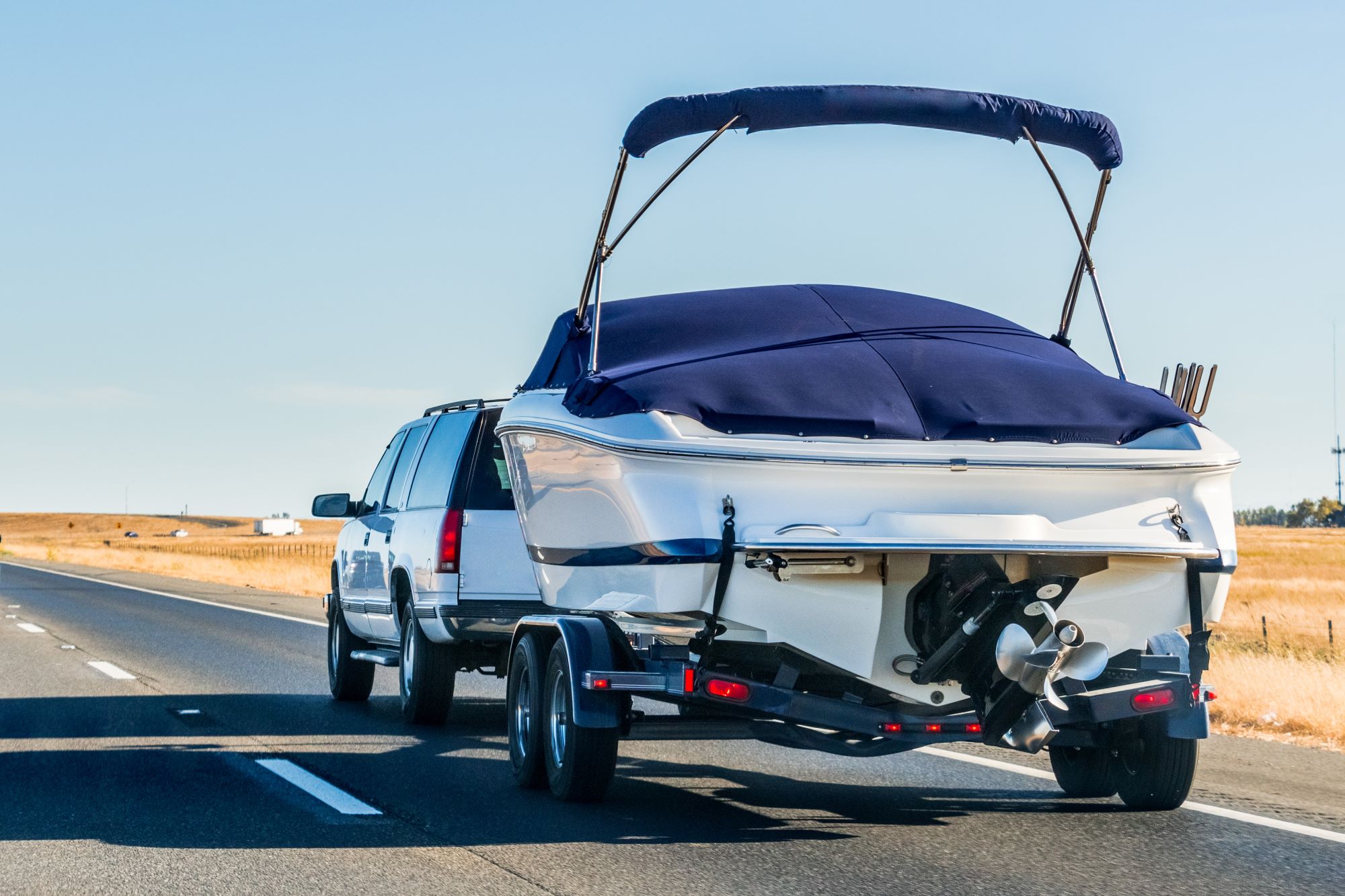 A SUV pulls a trailer with a boat on it on a highway. The boat and vehicle are white. 
