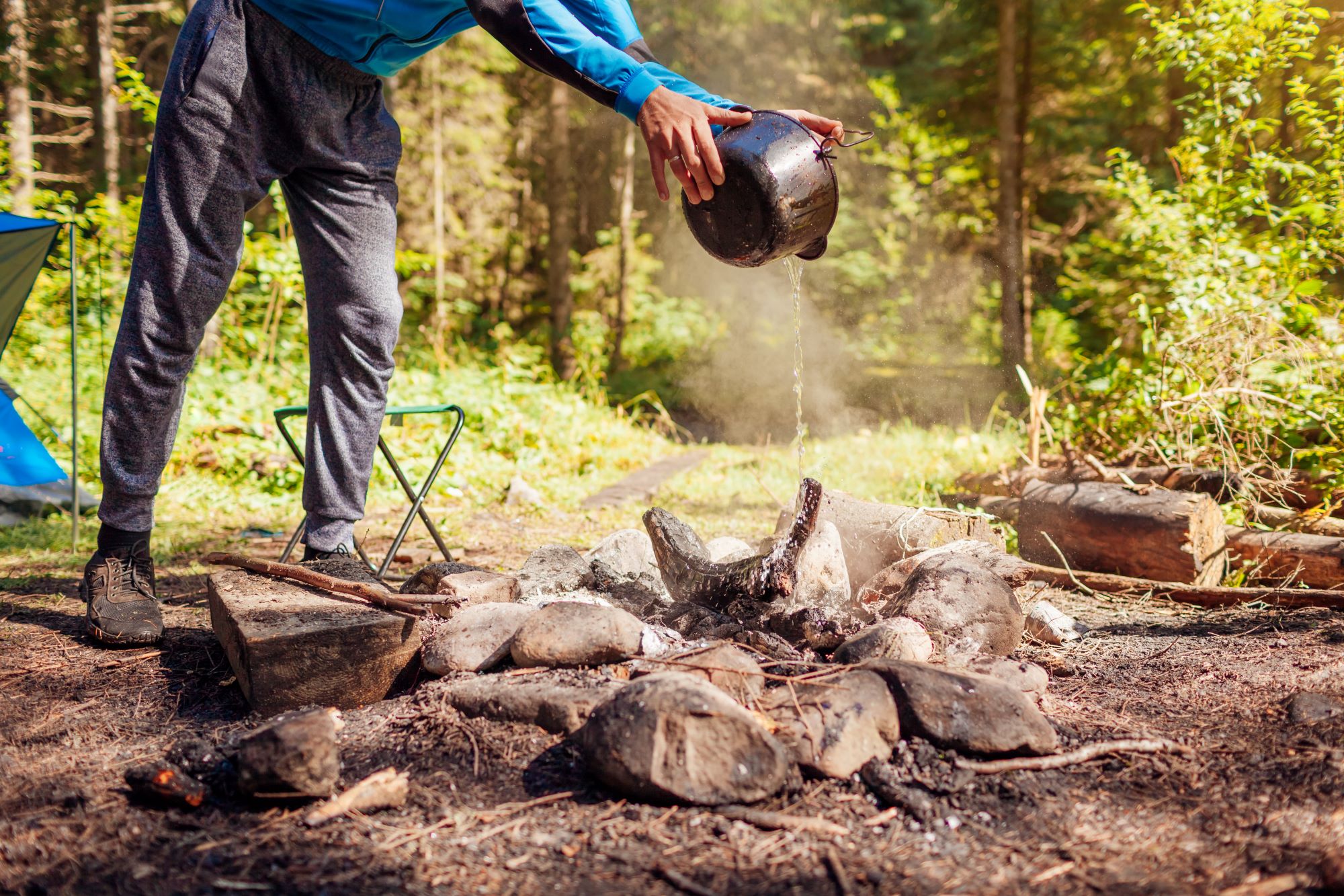 A person pours water on a campfire with a metal pan. 