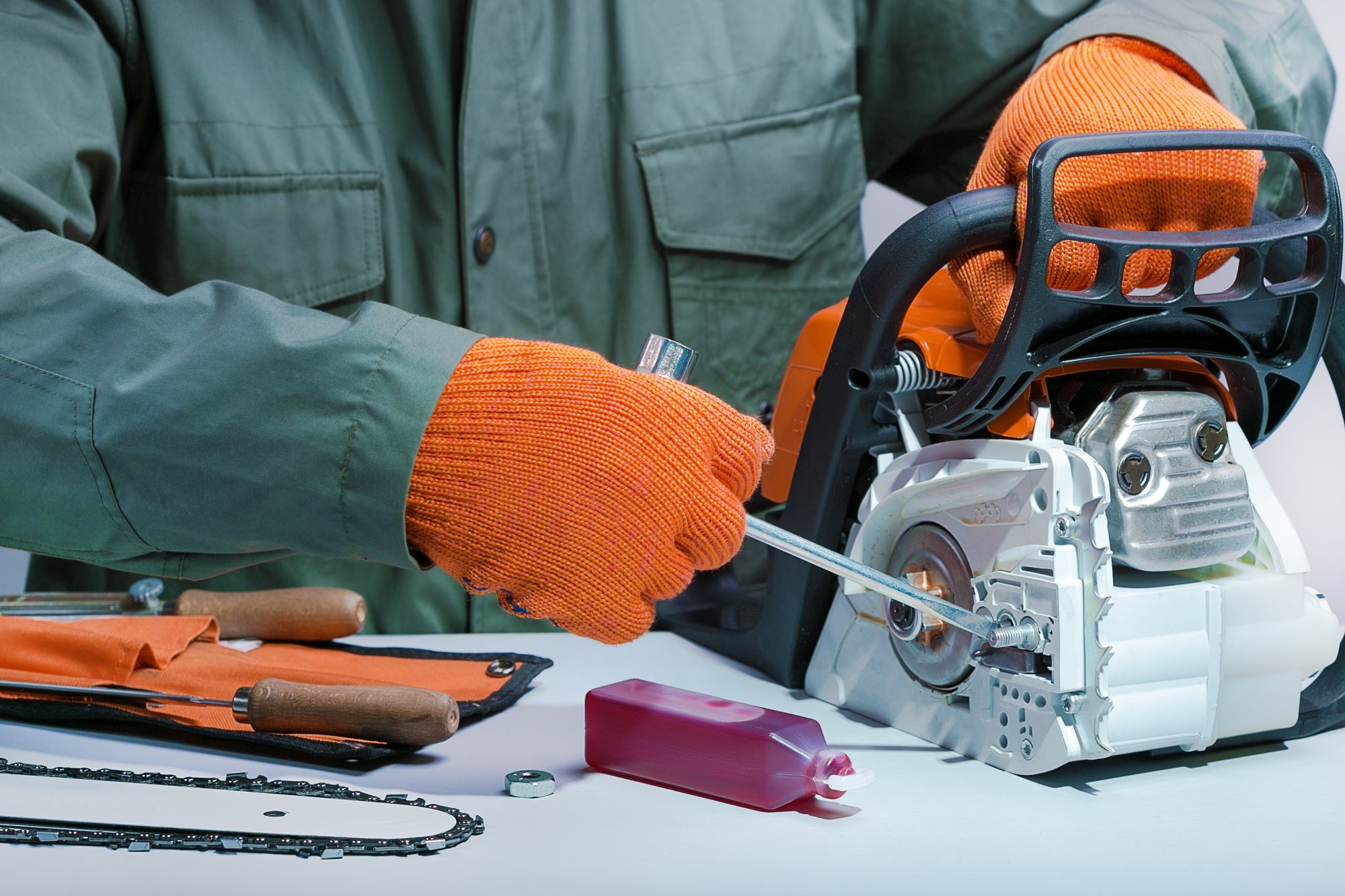 A person works on a chainsaw with a tool wearing gloves. 