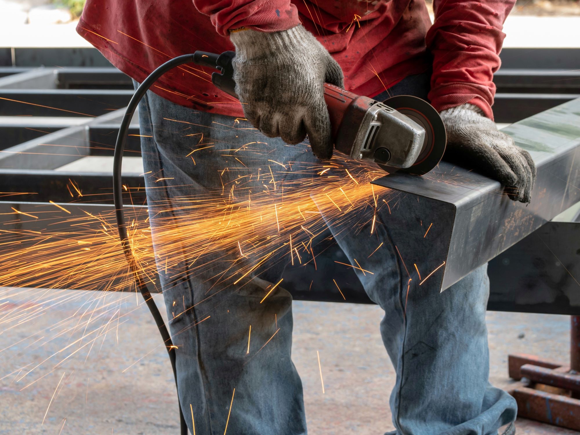 A person uses a grinding tool on a piece of metal. The tool is shooting sparks and the person is wearing gloves.