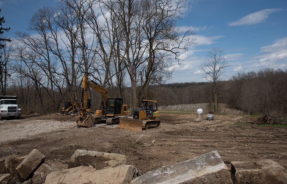 Construction vehicles on vacant plot where building once stood, newly planted trees in background.