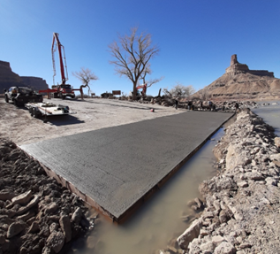 Construction vehicles sit on a concrete boat ramp surrounded by rocks.