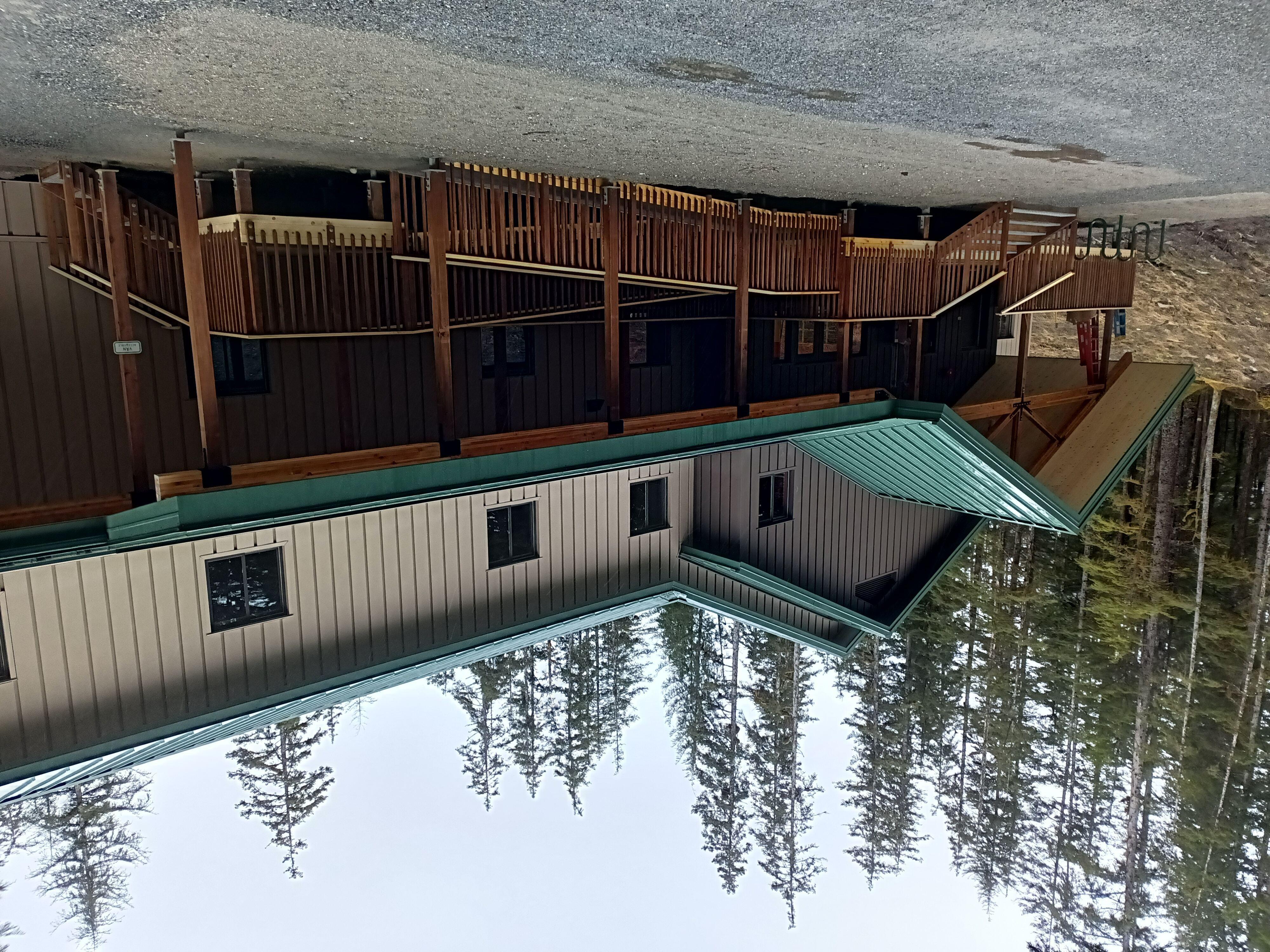 Two story housing building with tan siding and green roof.