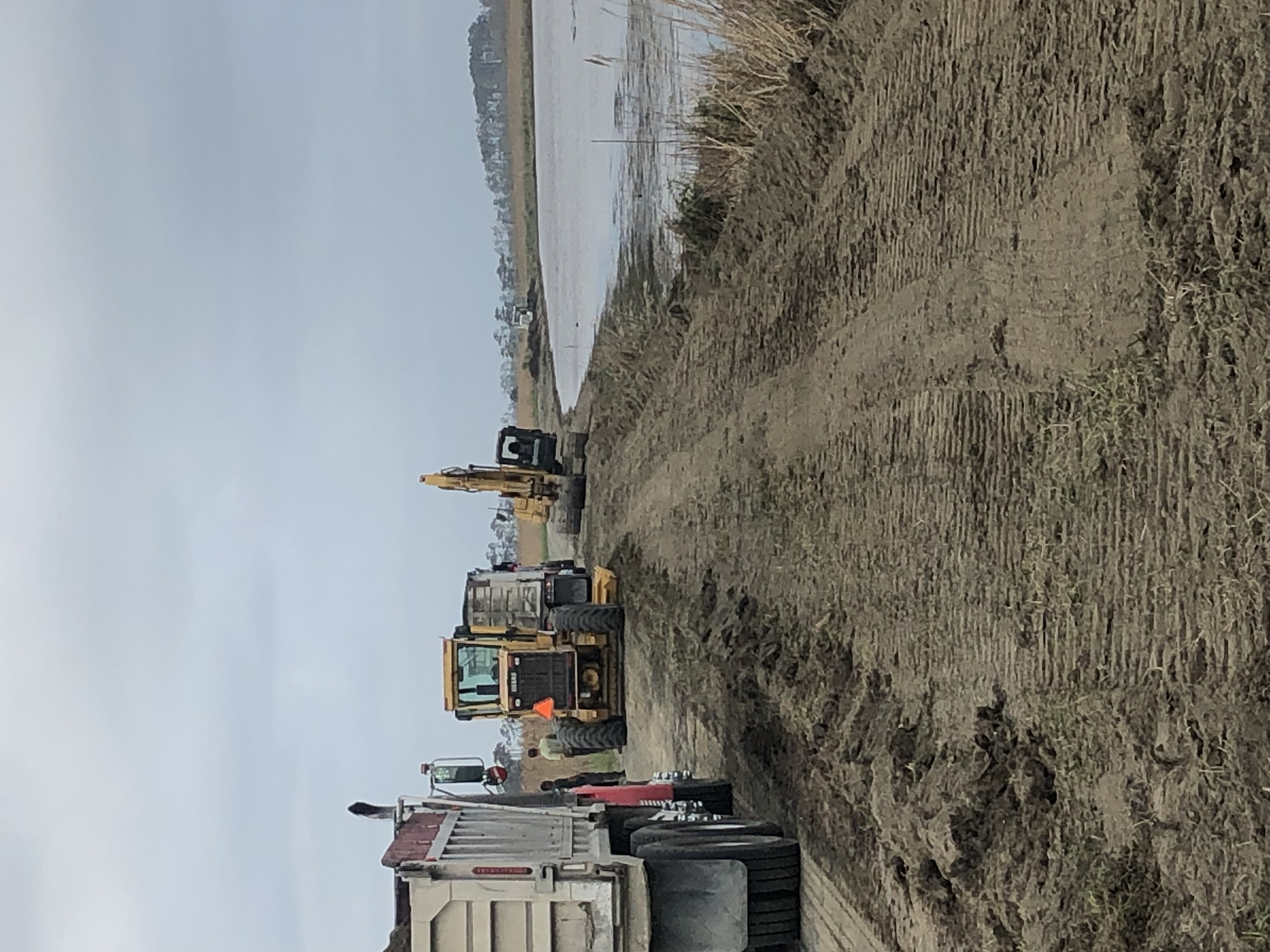 Construction vehicles sit alongside levee leading to a body of water.