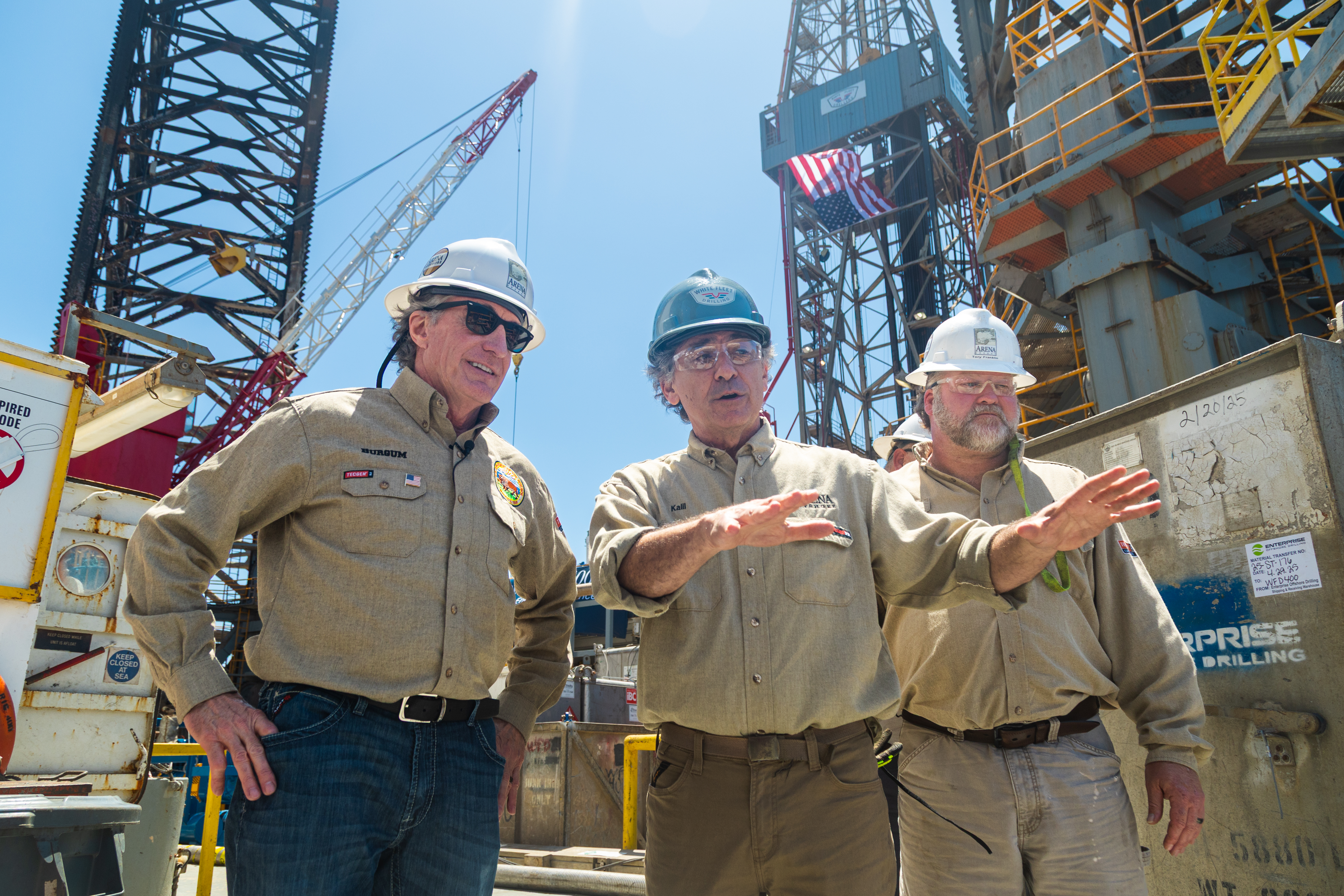 Secretary Burgum and two others in front of oil and gas rig.