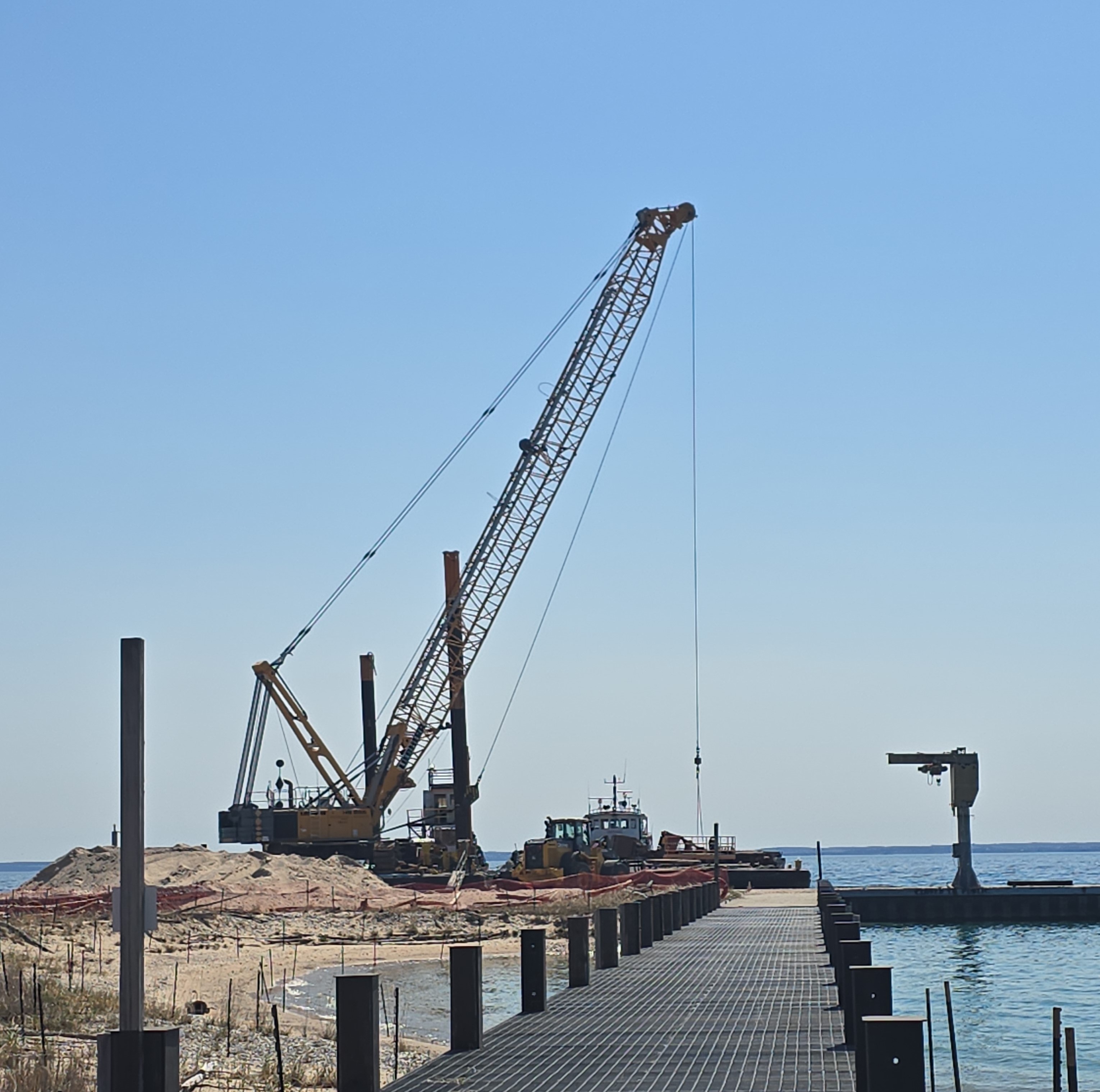 A large crane stands over a dock that extends into a blue lake.