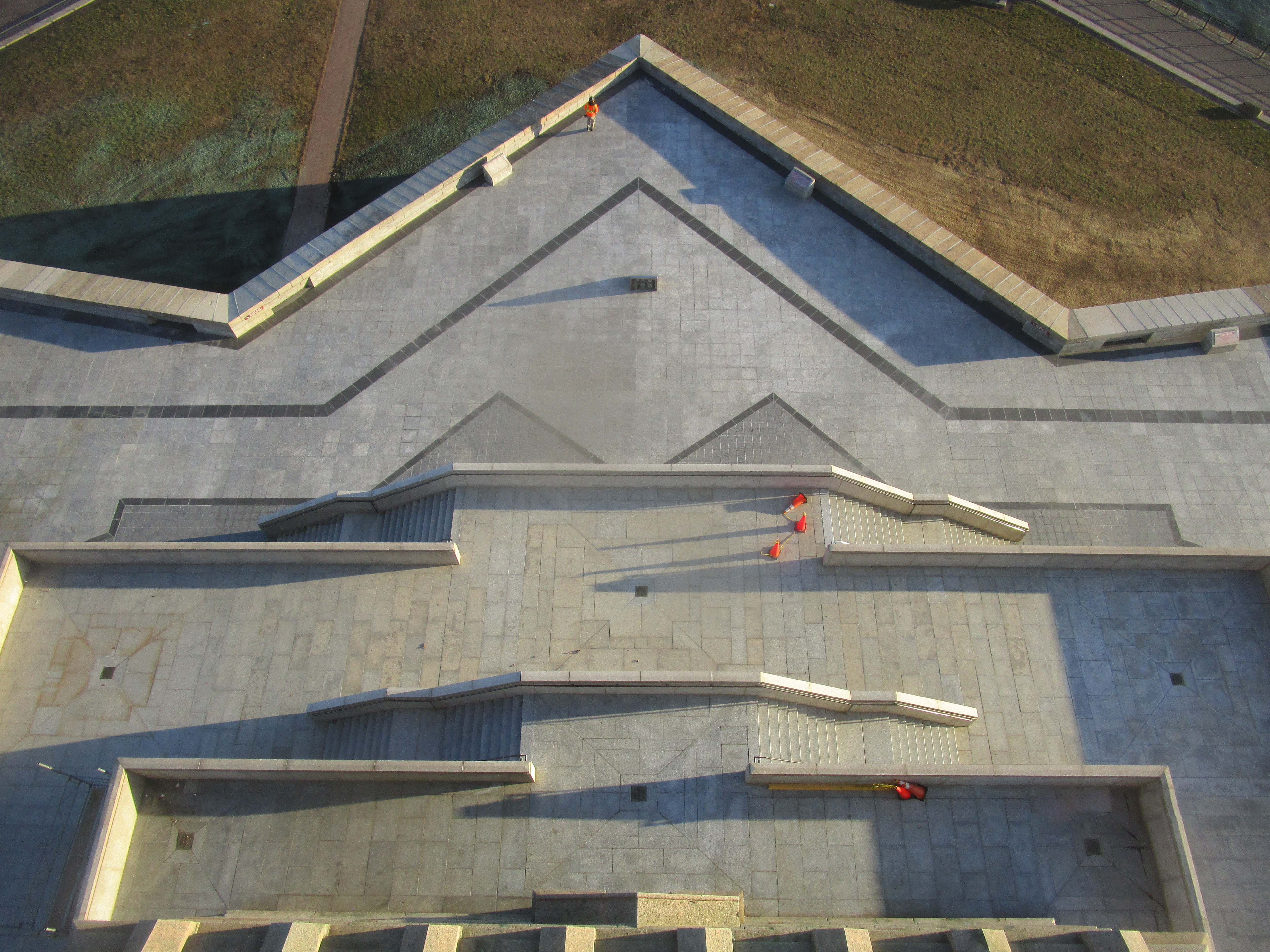 Overhead view of a completed stone-paved pedestrian area with terraced ramps and handrails forming a geometric layout.
