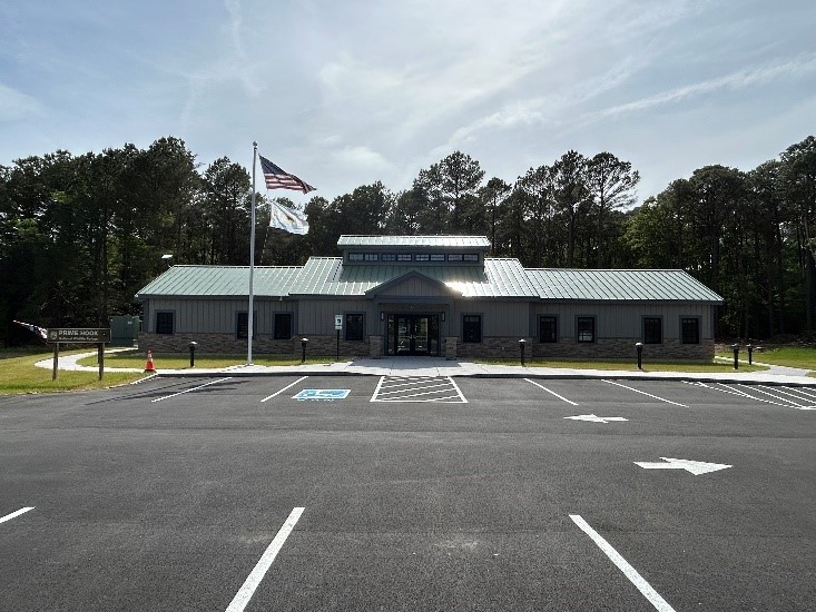  A newly constructed visitor contact station with a green metal roof sits behind a freshly paved parking lot with marked spaces. 