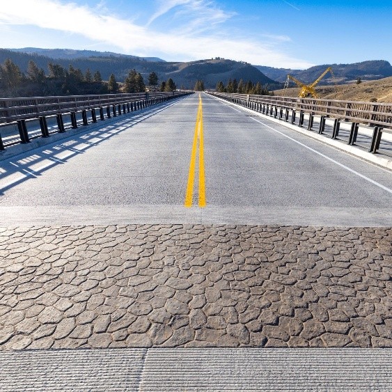 View from one end of the new Yellowstone River Bridge with fresh pavement and yellow center lines, set against a mountainous landscape.