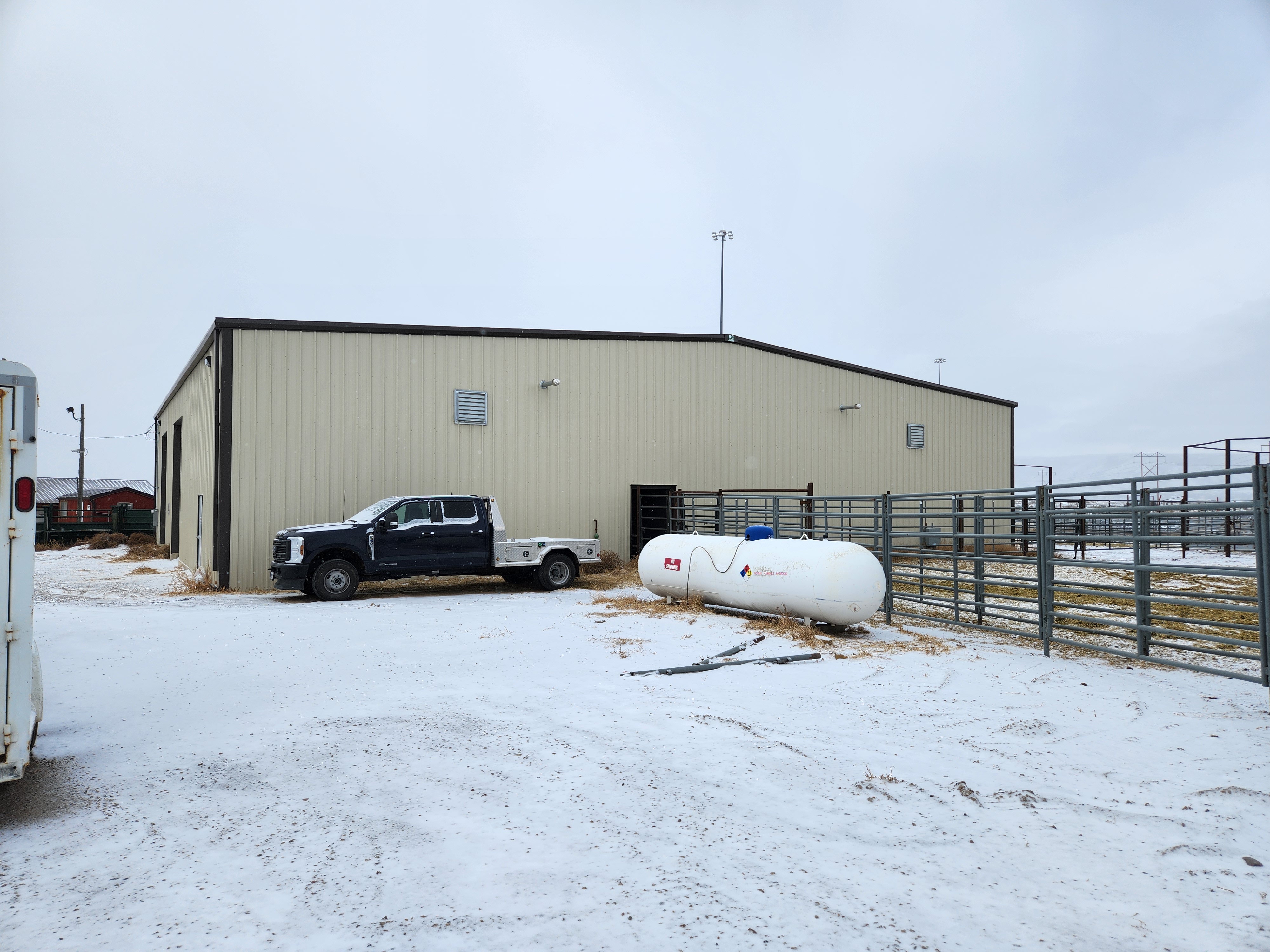 Exterior view of a new, beige metal chute facility with a pickup truck parked beside it, connected to a fenced area for livestock.