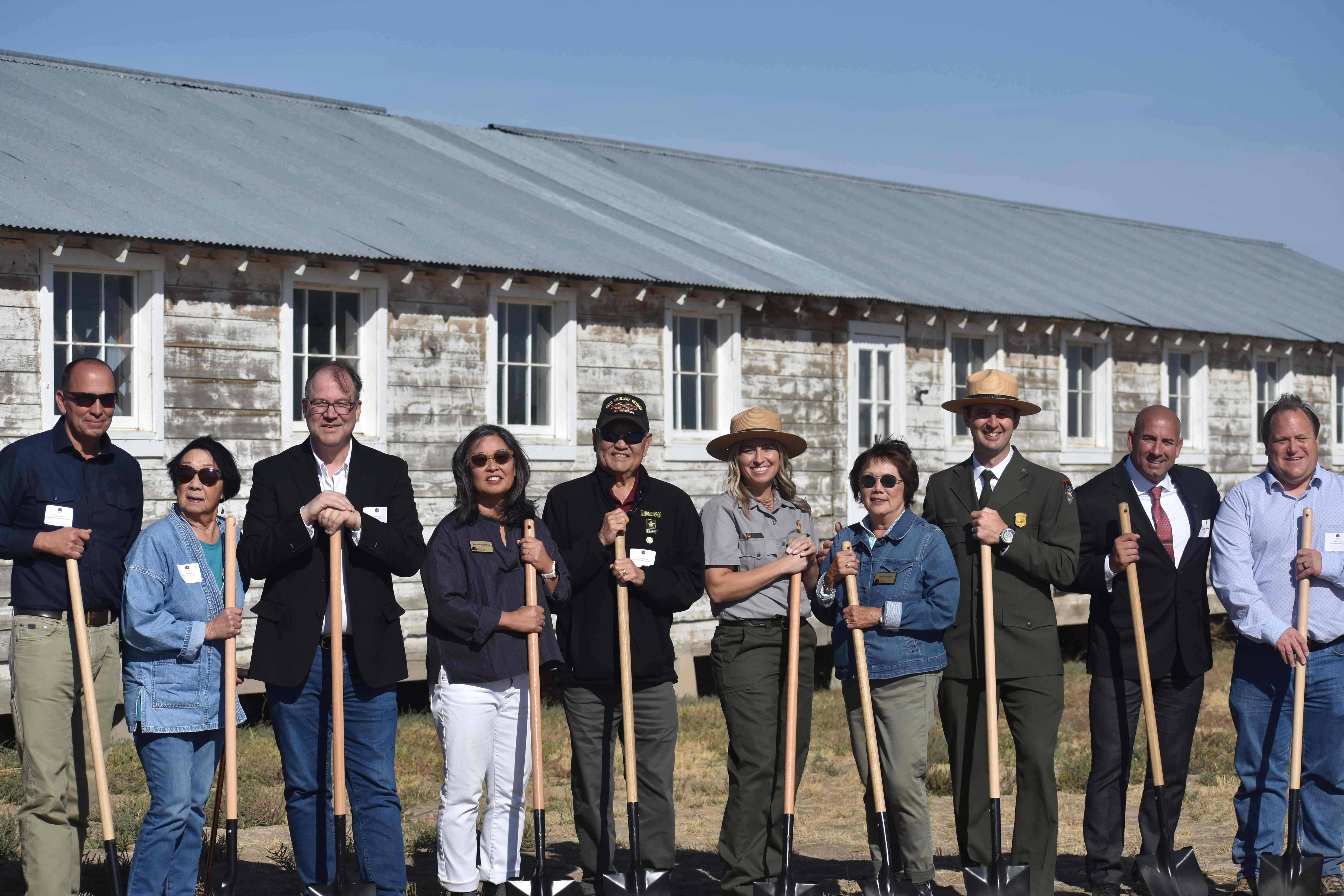 Group of officials holding ceremonial shovels in front of a historic building.