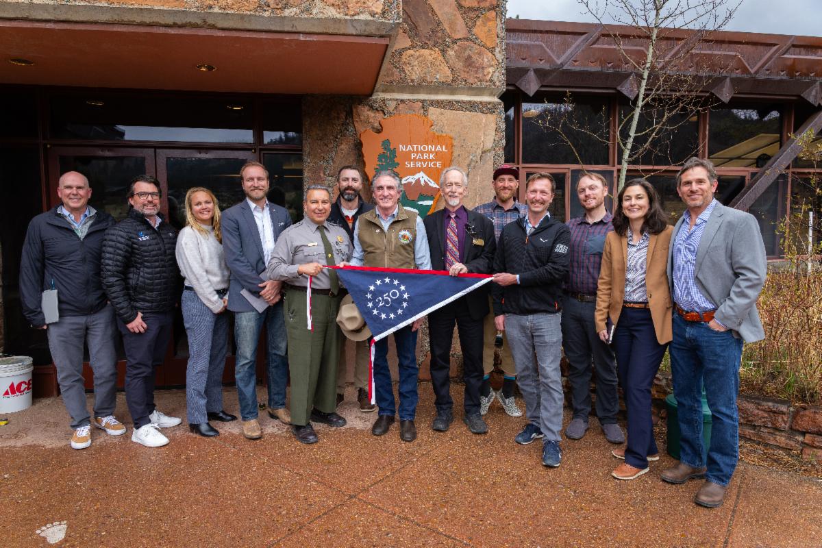Group holding 250 flag in front of NPS sign on stone building
