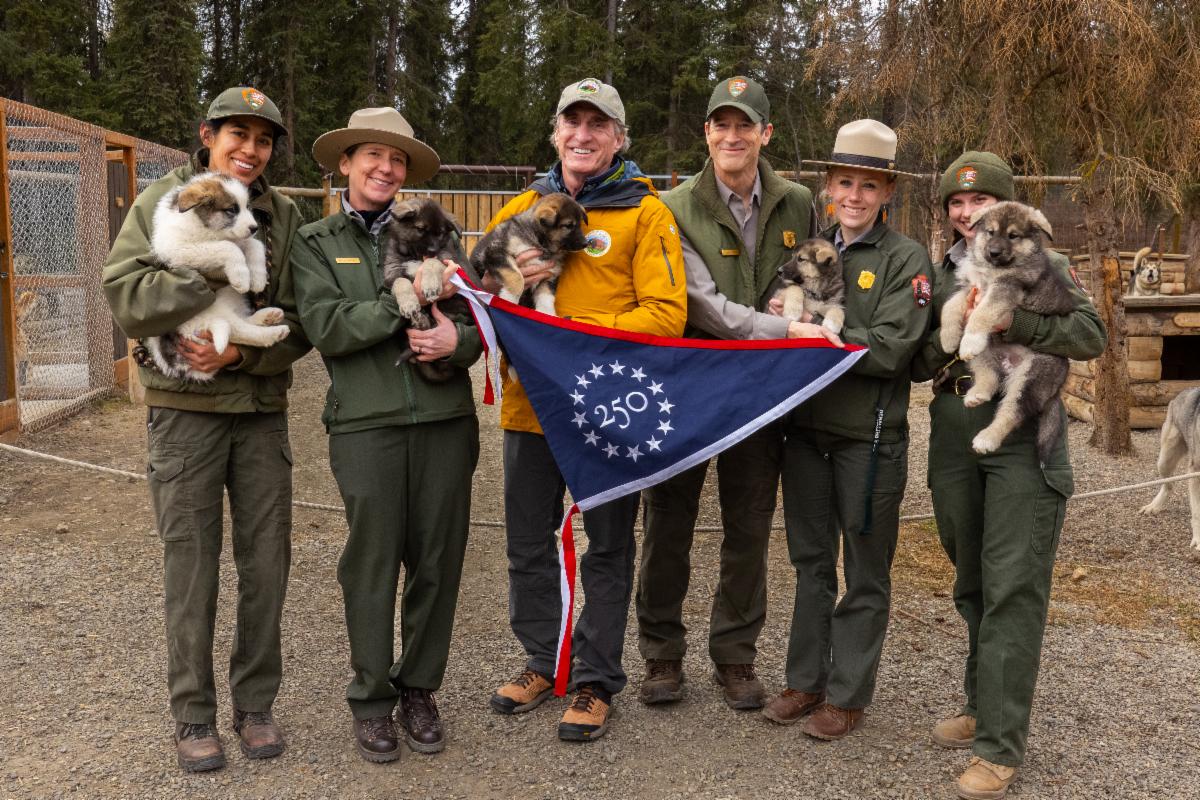 Secretary Burgum and NPS staff holding puppies and 250 flag. 