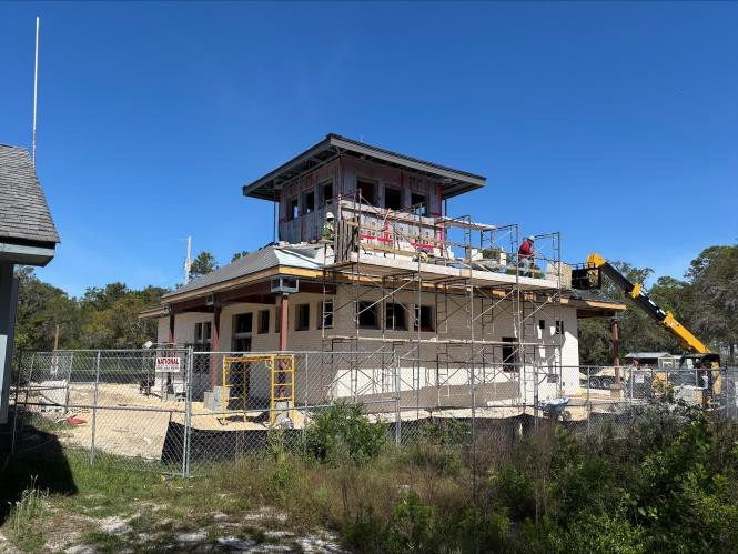 Two-story headquarters building under construction with scaffolding, surrounded by a fence.