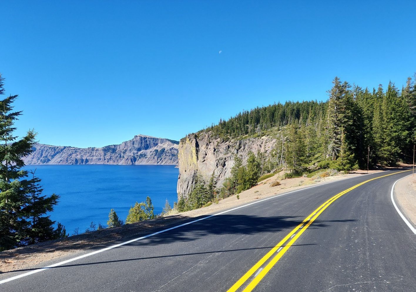 Freshly paved road with yellow double line and a view of Crater Lake in the background.