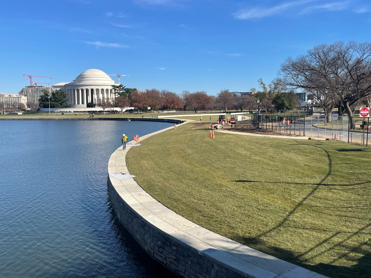 Jefferson Memorial across the Tidal Basin with a curved, stone seawall and grassy area.