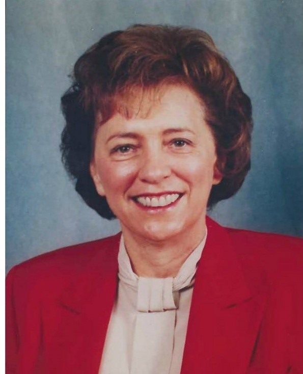 Kathy Karpan against a blue background. She is smiling and wearing a white blouse and a red blazer.