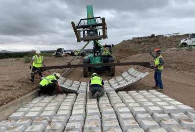 A construction crew uses a small crane and manpower to lay out mats to form a new road in a dirt site