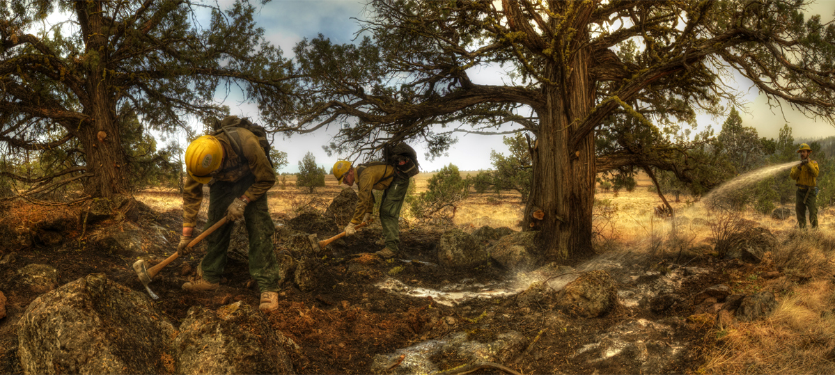 Firefighters stir and douse ashes with water.