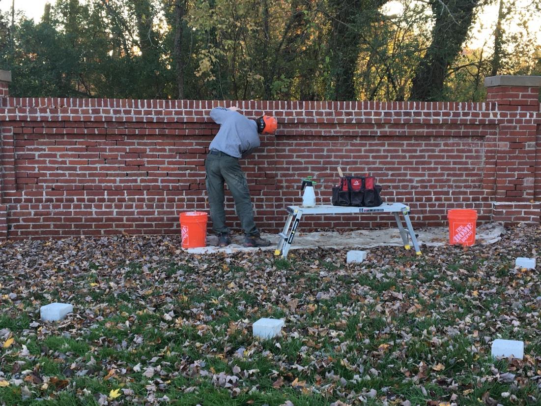 Maintenance Action Team worker repairing red brick wall in grass area.
