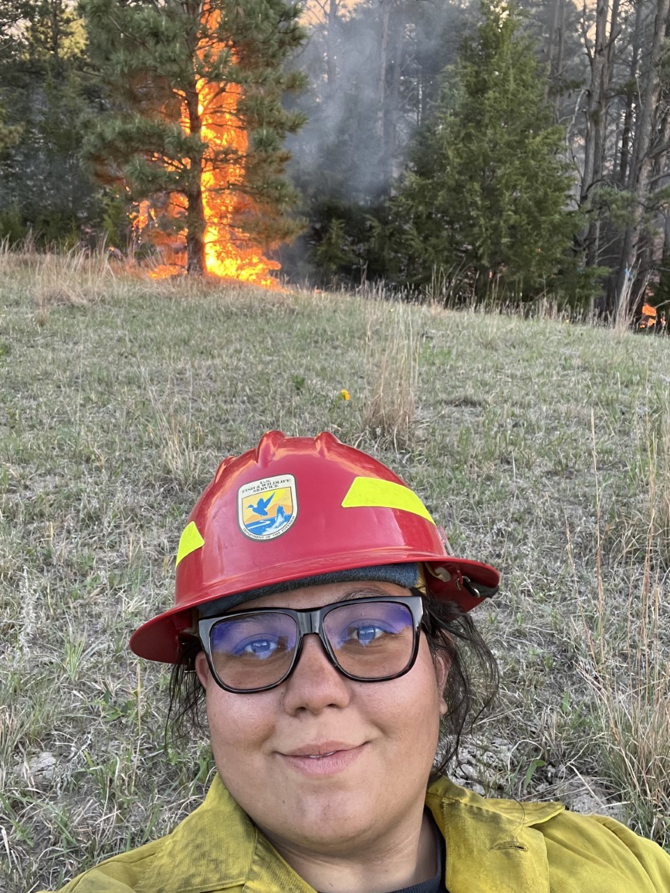 Saydee Marie Fujioka wearing wildland firefighter gear, holding a drip torch on a prescribed burn. 