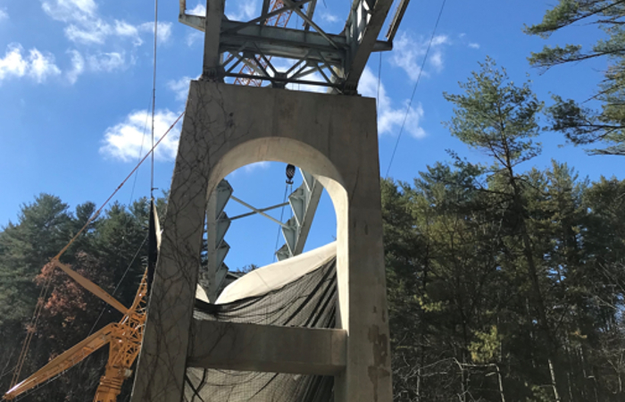 Unfinished bridge standing in front of heavy machinery and trees, underneath blue sky.