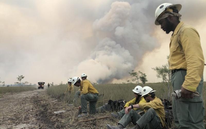 Jackson Hotshots beside a road with smoke billowing in the background.