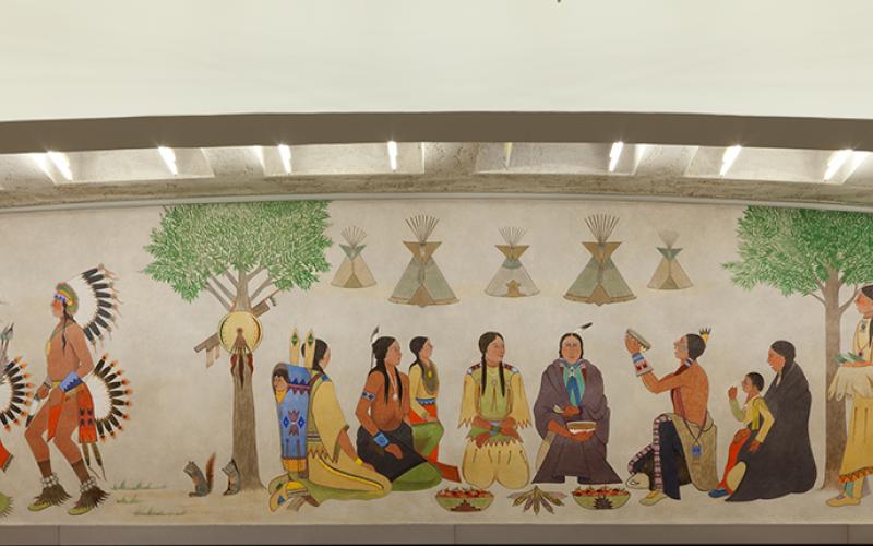 Kiowa dancers, drummers, and women preparing food frame the traditional harvest feast and Kiowa homes in the center of this painted lunette mural.