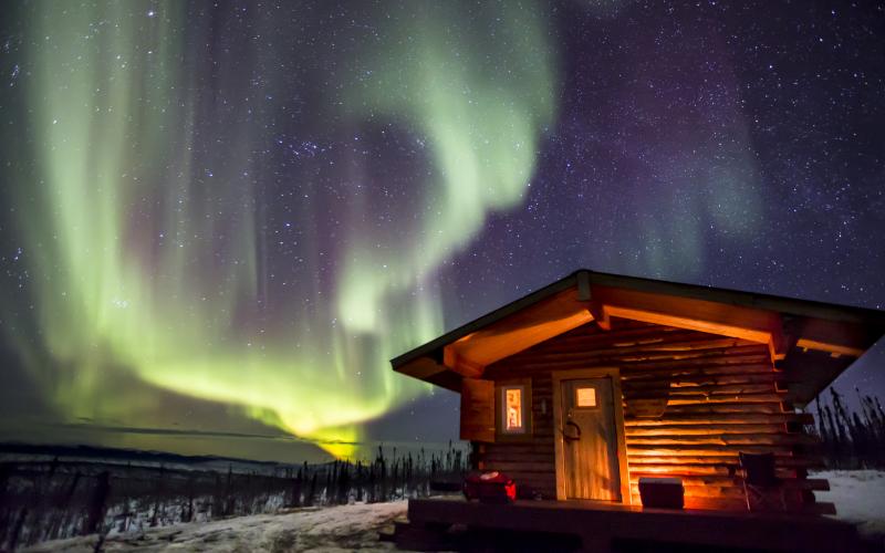 Wooden cabin under a starry sky with northern lights.