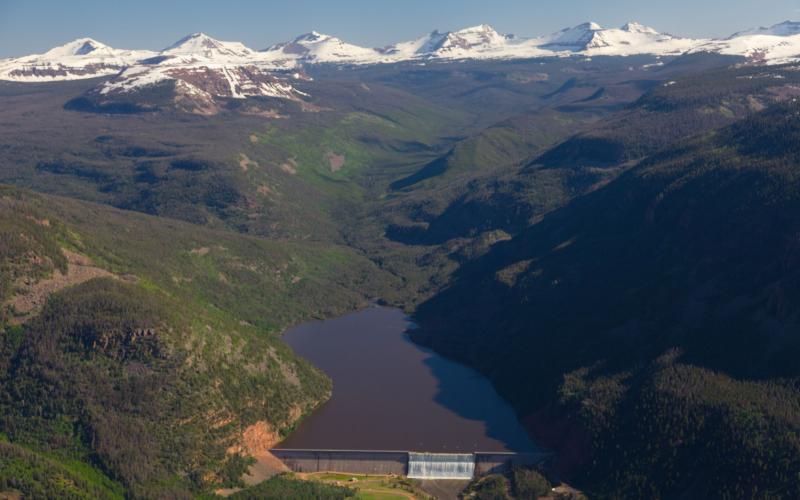 Aerial view of snow covered Uintah Mountains in the background with Upper Stillwater reservoir and dam in the foreground.