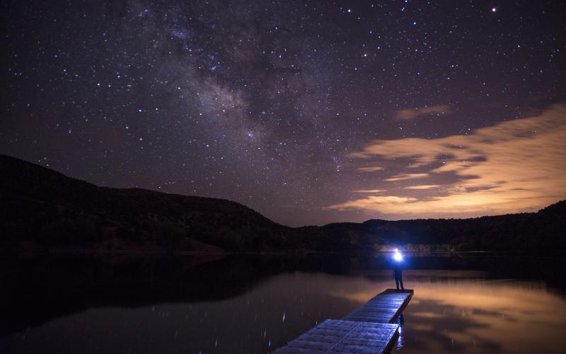 Person stands at the end of a dock under a starry sky.