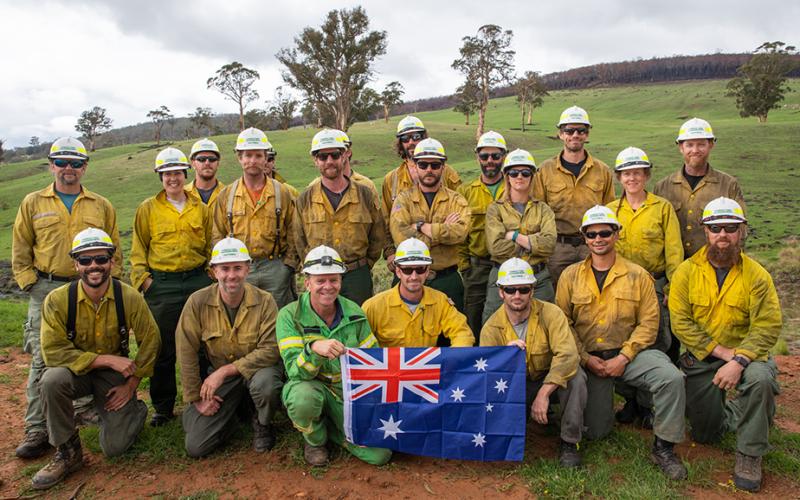 A group of American and Australian firefighters standing around an Australian flag