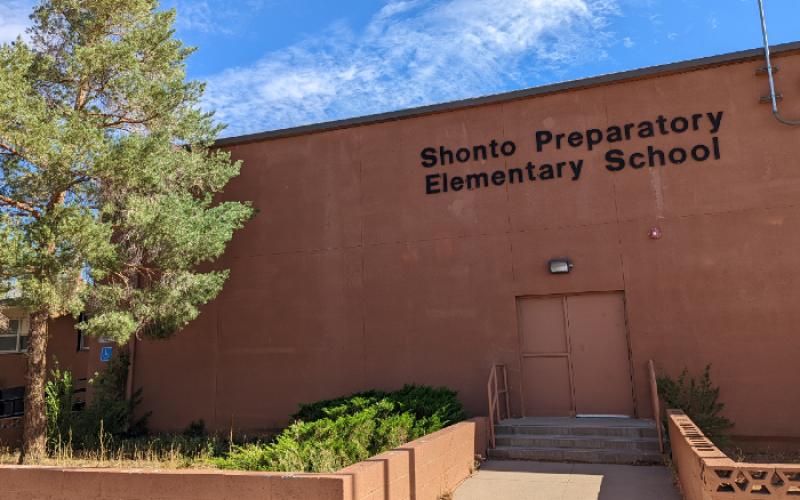A rust red school building with Shonto Preparatory Elementary School on it in black letters and a tree. 