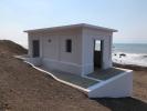 A small white building on a sandy cliff with the ocean behind it