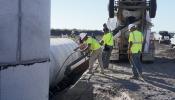 Men in construction vests place new concrete outlet pipes and cement them in place.